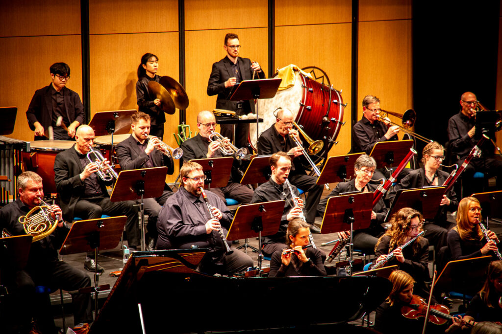 Orchester mit Musikern in schwarzen Anzügen spielt auf verschiedenen Instrumenten, Frontalansicht
