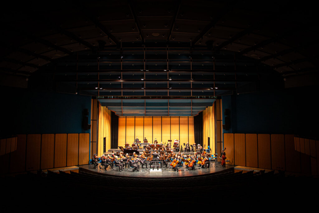 Orchester auf Bühne, warme Beleuchtung, von vorne gesehen